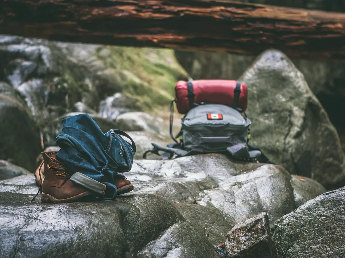 Hiking boots and a backpack resting on rocks beside a trail